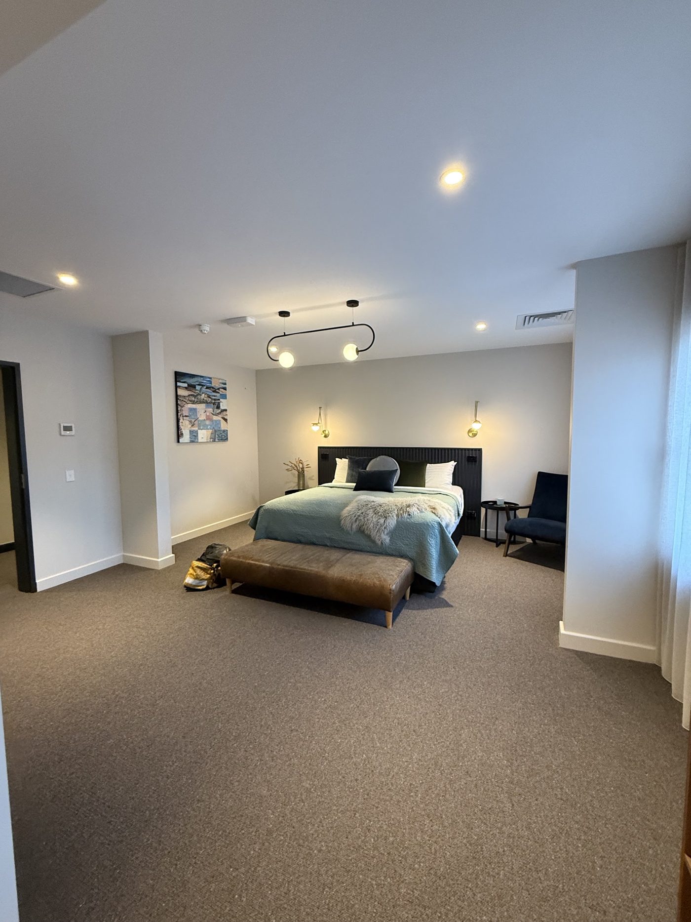 Bedroom lit by downlights, a pendant fitting and wall lights beside the bed