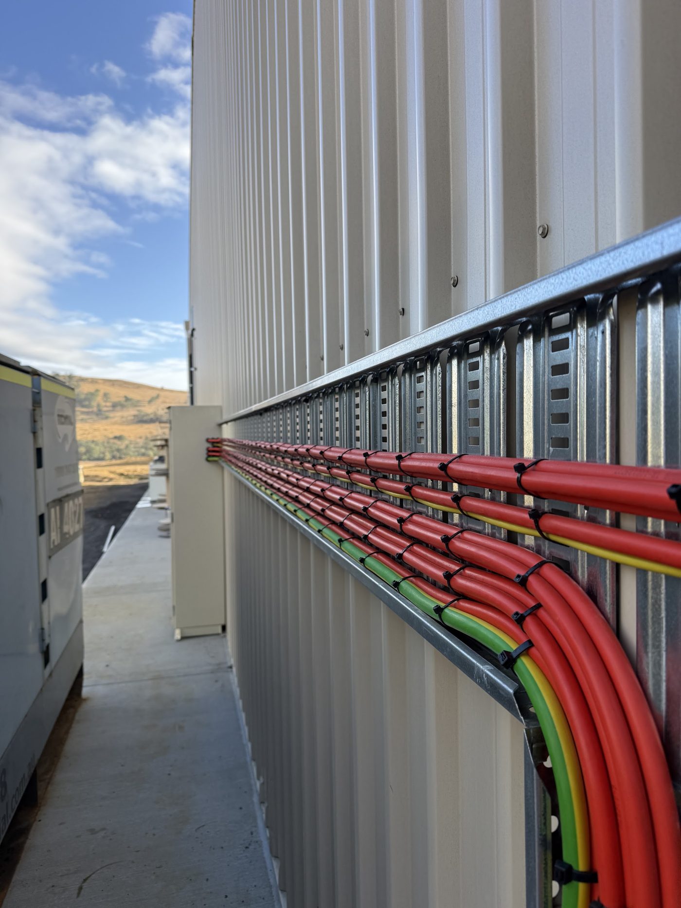 Red, green and yellow cables dressed along a cable tray on the outside wall of an industrial building