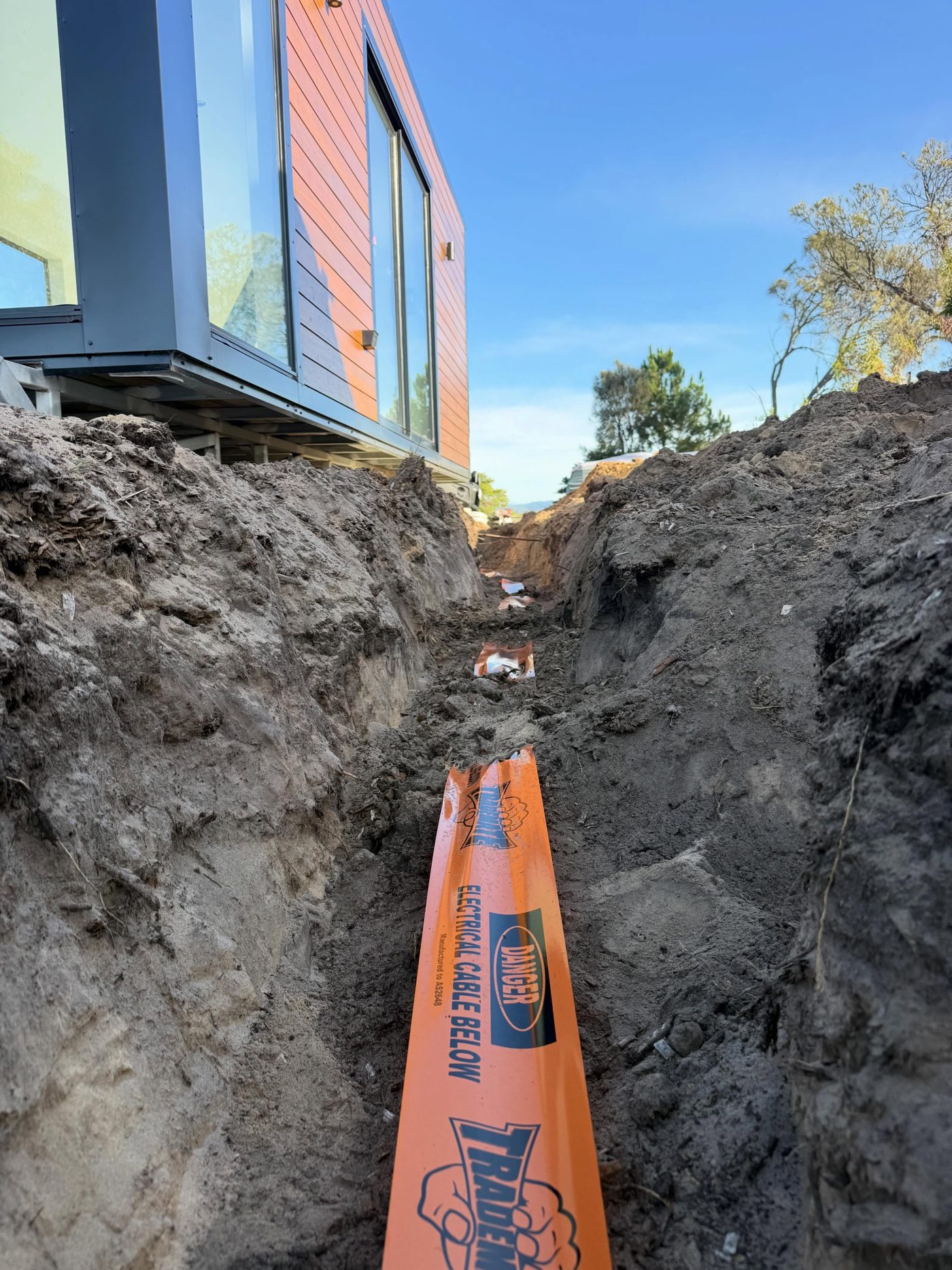 Trench with orange electrical cable danger tape below a new tiny home