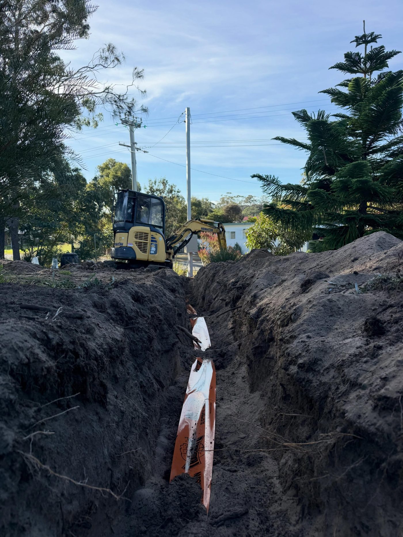 The same trench from further back with a mini excavator and power poles behind