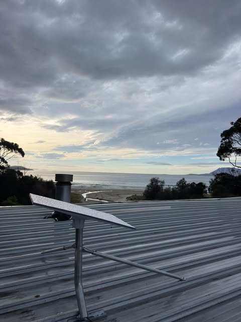Pole mounted panel on a metal roof with the water and hills behind at dusk